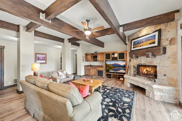 Exposed stained wood ceiling beams, corner natural stone fireplace with a thick timber mantel, built-in wooden cabinetry, and wood-finish flooring