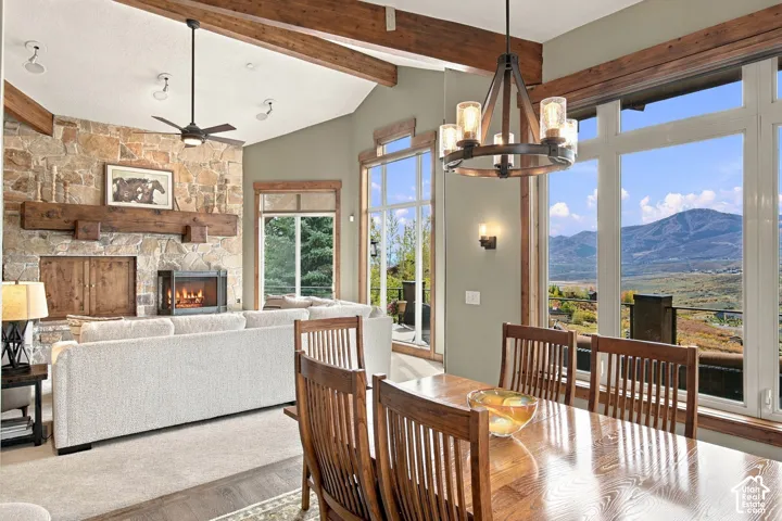Vaulted ceilings featuring exposed timber beams, full-height stone fireplace with a thick timber mantel, and floor-to-ceiling windows with mountain scenery
