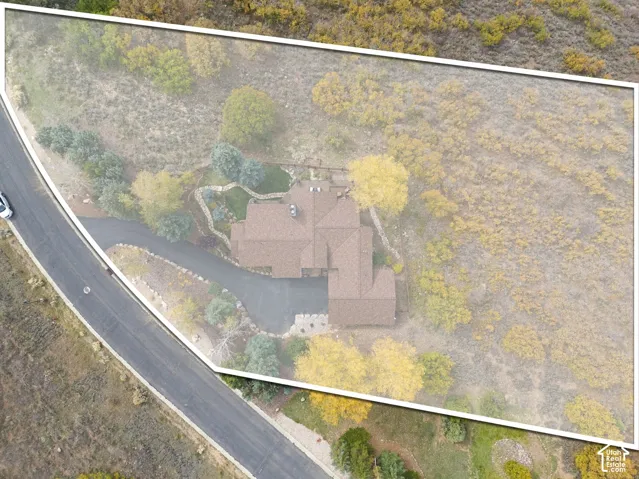 Aerial perspective of a multi-gabled residence featuring an asphalt driveway, stone pathway, and mature vegetation on a sloped lot