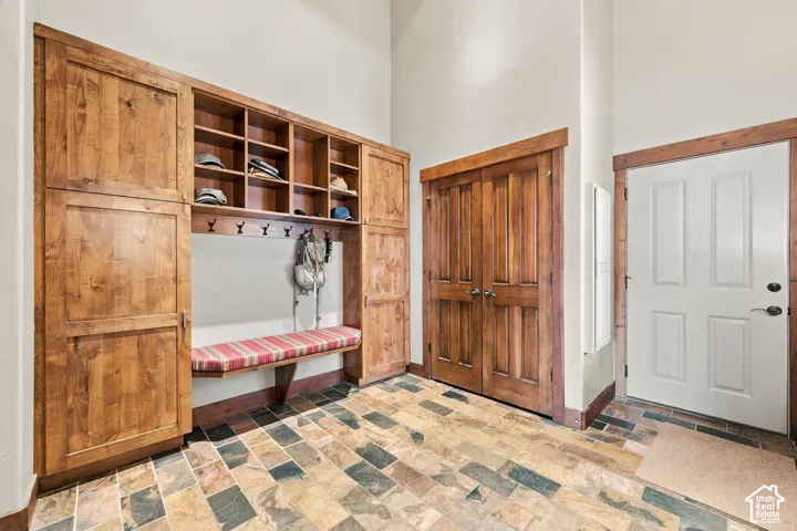 Mudroom featuring built-in wood cabinetry, integrated storage cubbies, wall-mounted coat hooks, and multi-tonal stone tile flooring