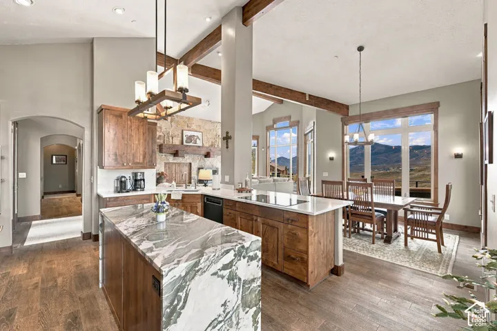 Kitchen featuring custom wood cabinetry, natural stone waterfall-edge island, vaulted ceilings with exposed wood beams, and mountain scenery framed by expansive windows