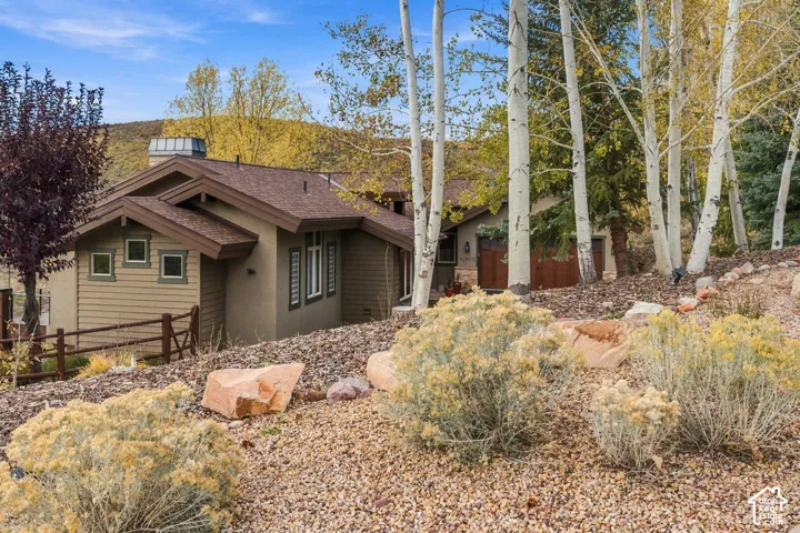 Exterior featuring horizontal siding, a multi-gabled shingle roof, integrated wood-finish garage doors, and natural stone landscaping elements, framed by mature aspen trees