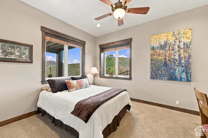 Neutral-toned interior featuring stained wood window casings, a multi-blade ceiling fan with integrated lighting, wall-to-wall carpeting, and natural mountainous scenery