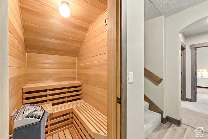 Sauna featuring wood-plank walls, tiered built-in wood slat bench seating, and an integrated heating unit