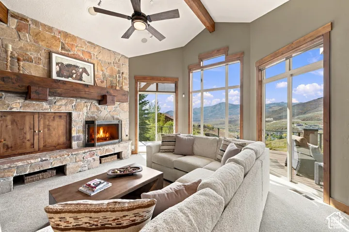 Floor-to-ceiling stone fireplace with a thick timber mantel, vaulted ceilings with exposed wood beams, expansive floor-to-ceiling windows, and mountain scenery