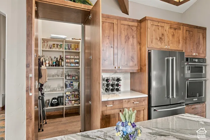 Custom wood cabinetry, stainless steel double wall ovens, stainless steel refrigerator, stone-surfaced kitchen island, and concealed walk-in pantry
