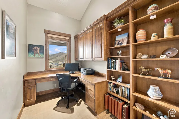 Custom-built stained wood cabinetry featuring an L-shaped desk surface, overhead storage units, and integrated floor-to-ceiling shelving, complemented by a vaulted ceiling and mountain scenery