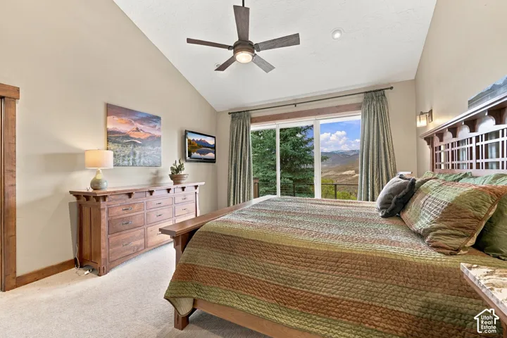 Vaulted ceilings featuring a central paddle fan, sliding glass doors, carpeted flooring, and mountain scenery