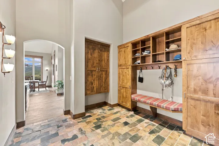 Built-in wooden cabinetry featuring open cubbies and enclosed storage, wall-mounted light fixtures, arched doorway, and multi-toned stone tile flooring