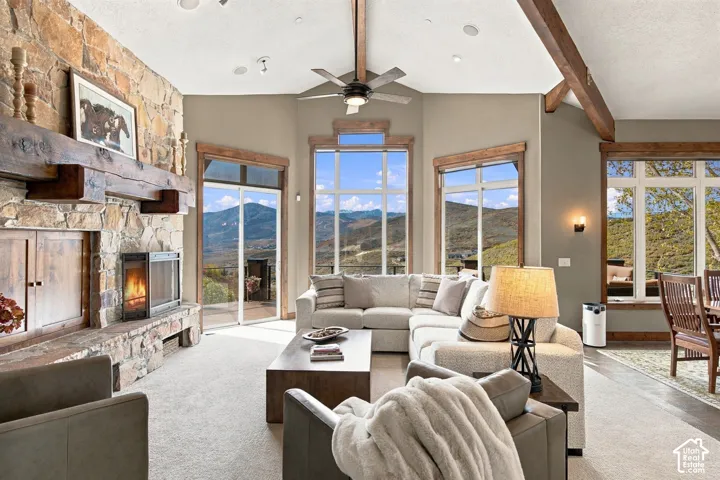 Living area featuring floor-to-ceiling stone fireplace with timber mantel, vaulted ceiling with exposed wood beams, and expansive windows showcasing mountain scenery