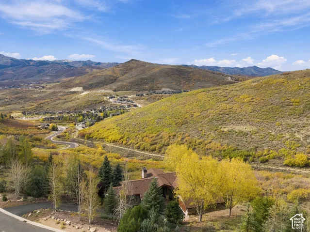Aerial perspective of a multi-level residence featuring shingle roofing, stone masonry, a chimney, and expansive mountain terrain