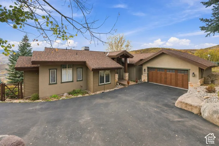 Exterior featuring horizontal siding, stone veneer accents, multi-gabled roofline, three-car garage with wood-style doors, and asphalt driveway