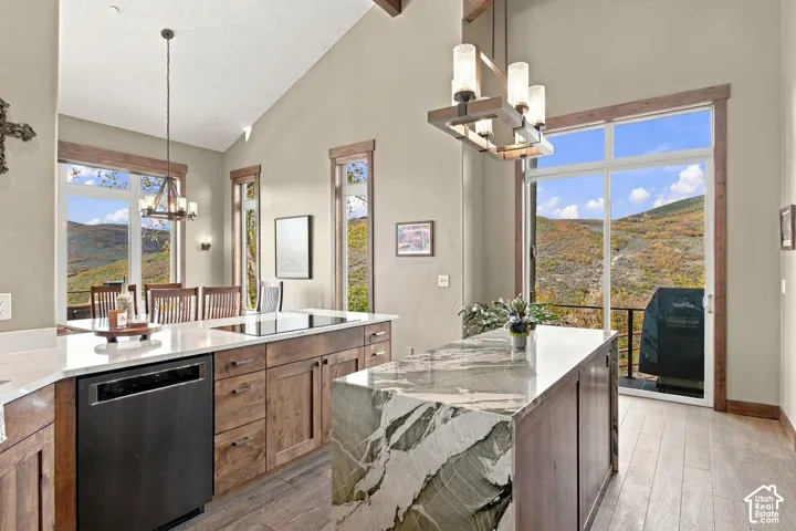 Kitchen featuring vaulted ceilings, a waterfall-edge stone island, wood-finish cabinetry, wood-finish flooring, and natural mountain scenery