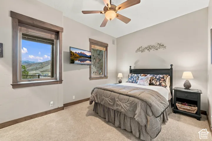 Neutral-toned room featuring expansive mountain scenery through double-pane windows, natural stone exterior wall accents, wood-trimmed window casings, and a ceiling-mounted light fixture with integrated fan