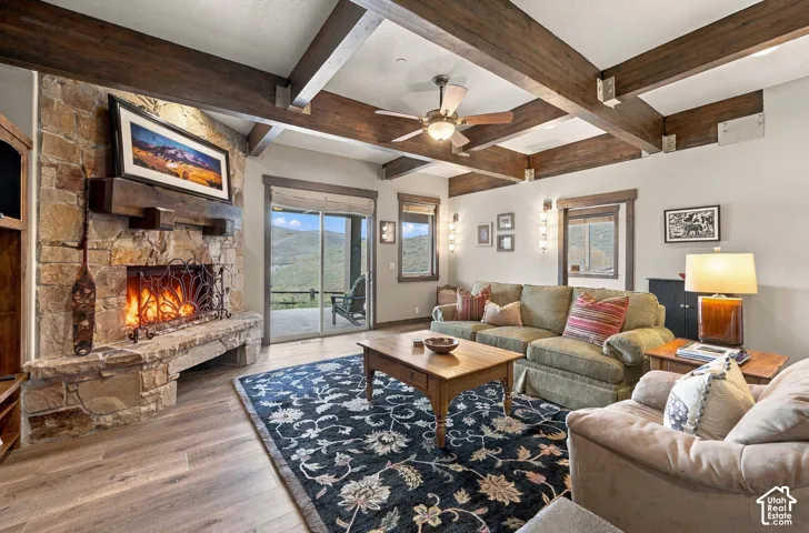 Great room featuring exposed timber ceiling beams, a floor-to-ceiling stone fireplace with a substantial wood mantel, wood-finish flooring, and sliding glass doors