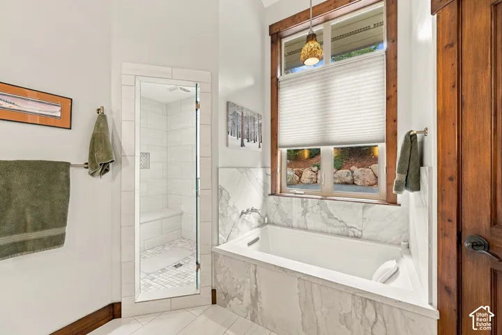 Soaking tub featuring stone-finish tile surround, glass-enclosed walk-in shower with tile interior, wood-trim windows, and solid wood door