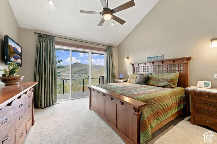 Vaulted ceiling, sliding glass doors, wall-mounted light fixtures, ceiling fan with integrated lighting, and mountain scenery