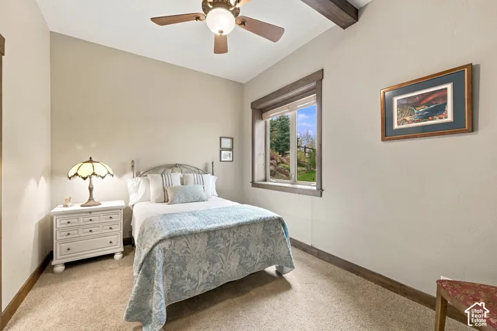 Room featuring neutral wall tones, a wood-trimmed window, ceiling fan with integrated lighting, and exposed ceiling beam