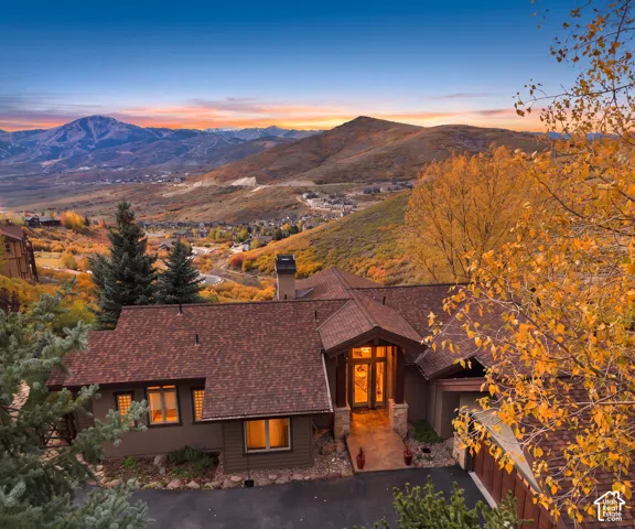Stucco exterior with stone detailing, shingle roof, covered entryway, and asphalt driveway, featuring a mountain backdrop