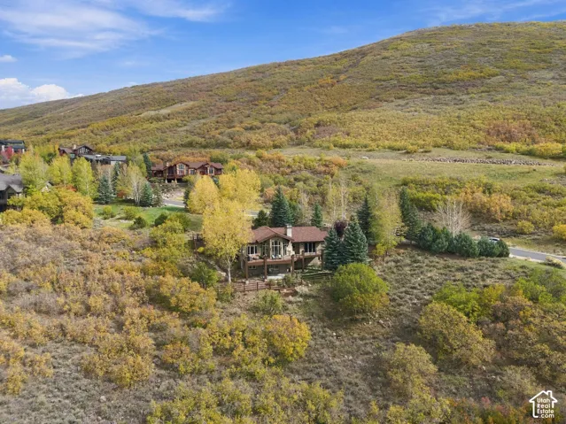 Mountain residence featuring multi-level wooden decking, stone exterior accents, a shingled roof, and an expansive sloped lot with mature trees