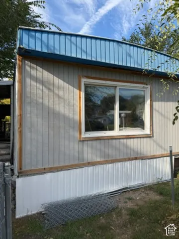 Exterior featuring vertical panel siding, blue metal roof trim, white metal skirting, and a large sliding window with wood-finish trim