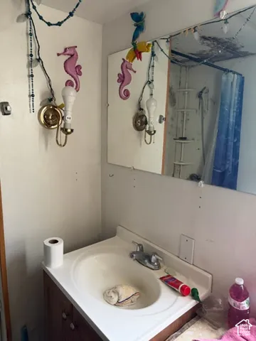 Bathroom vanity featuring a molded sink basin, double-handle faucet, wood-finish cabinetry, and a wall-mounted mirror with brass-tone light fixture