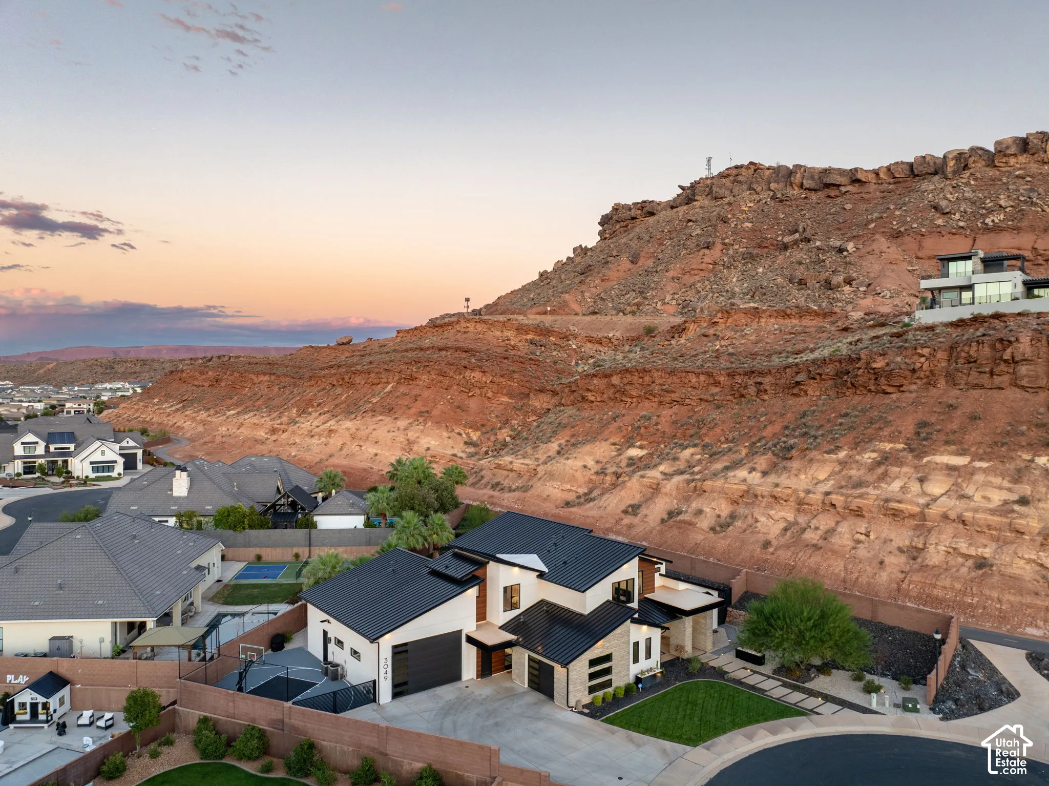 Contemporary residence featuring a multi-level metal roof, stone veneer accents, multi-car garage, and landscaped front yard set against a rock formation backdrop