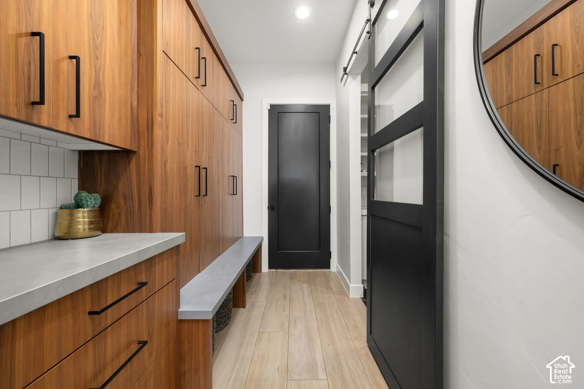 Built-in cabinetry with wood-finish doors and matte black hardware, concrete-style countertops, wood-finish tile flooring, sliding barn door with glass panes, and solid-panel door with matte black finish