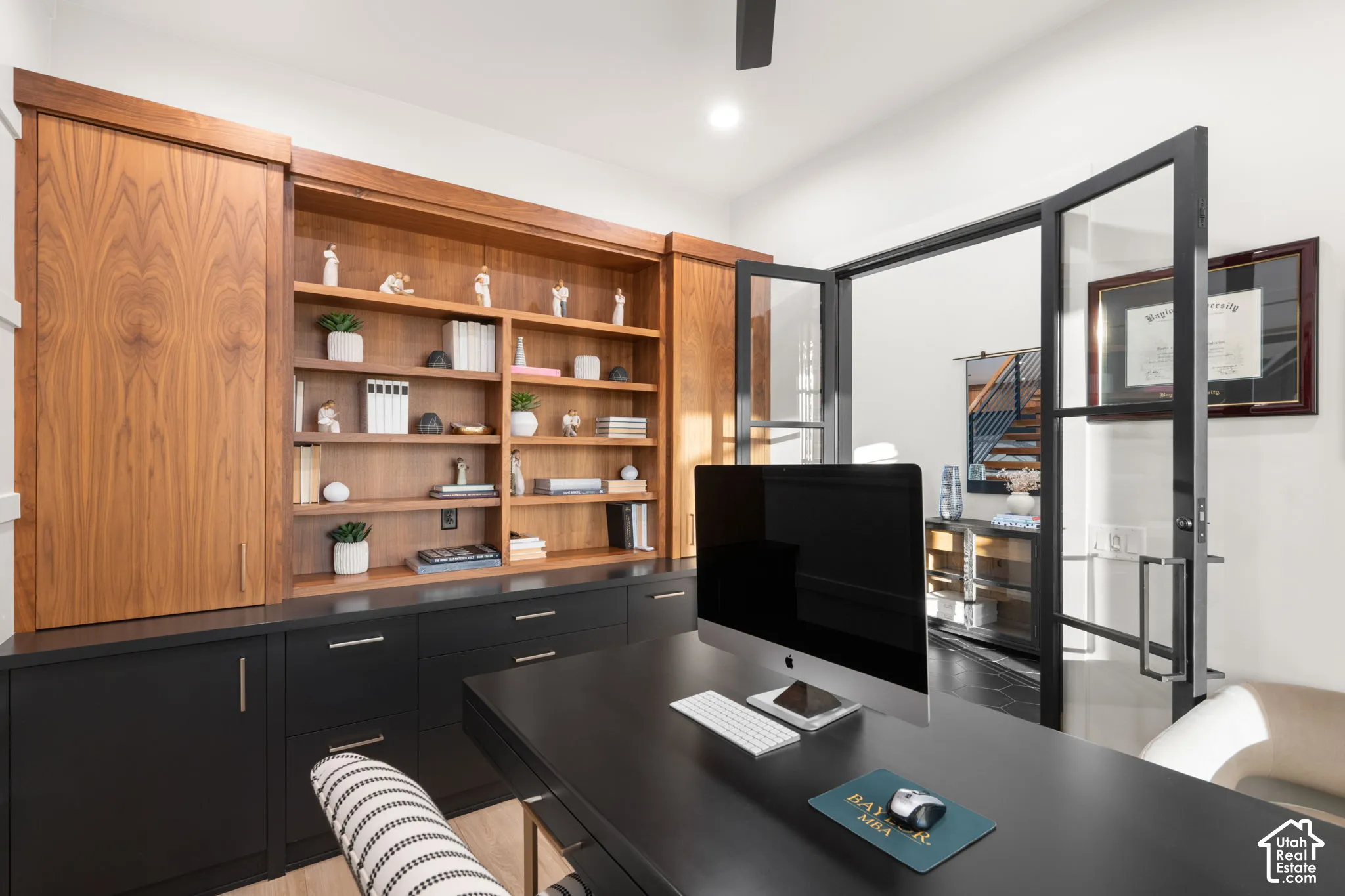 Custom built-in cabinetry with natural wood shelving and matte black lower storage, complemented by black-framed glass swing doors and a ceiling-mounted fan