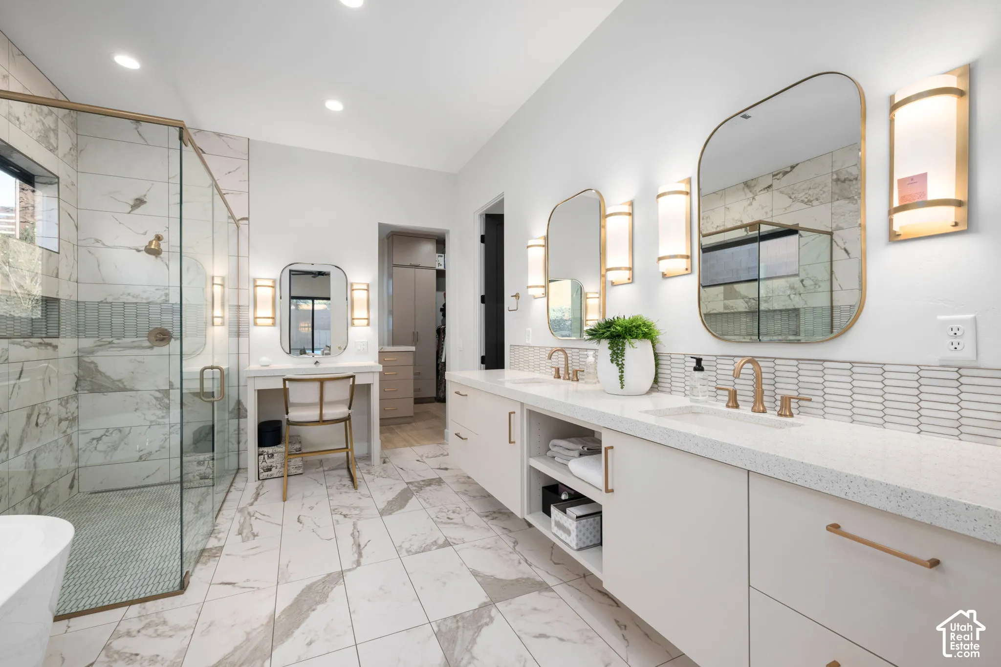 Double vanity with light-toned cabinetry, quartz countertops, dual integrated sinks, gold-tone hardware, and floor-to-ceiling tiled shower with glass enclosure