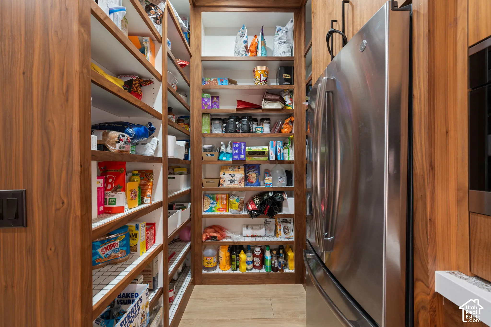 Custom wood-finish shelving, floor-to-ceiling cabinetry, and integrated stainless steel refrigerator