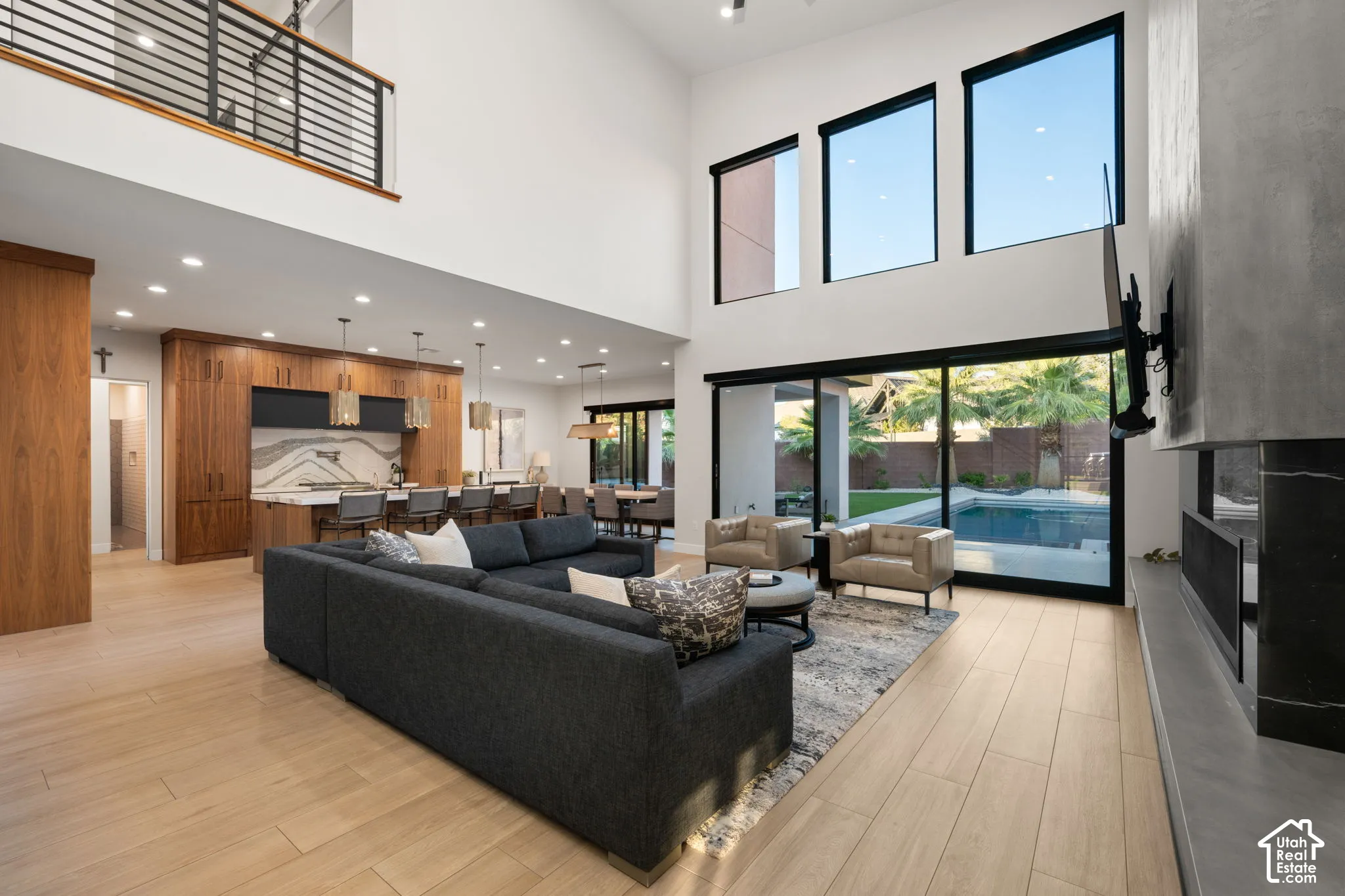 Double-height living area featuring floor-to-ceiling windows, wood-finish flooring, a full-height concrete fireplace surround, and recessed lighting