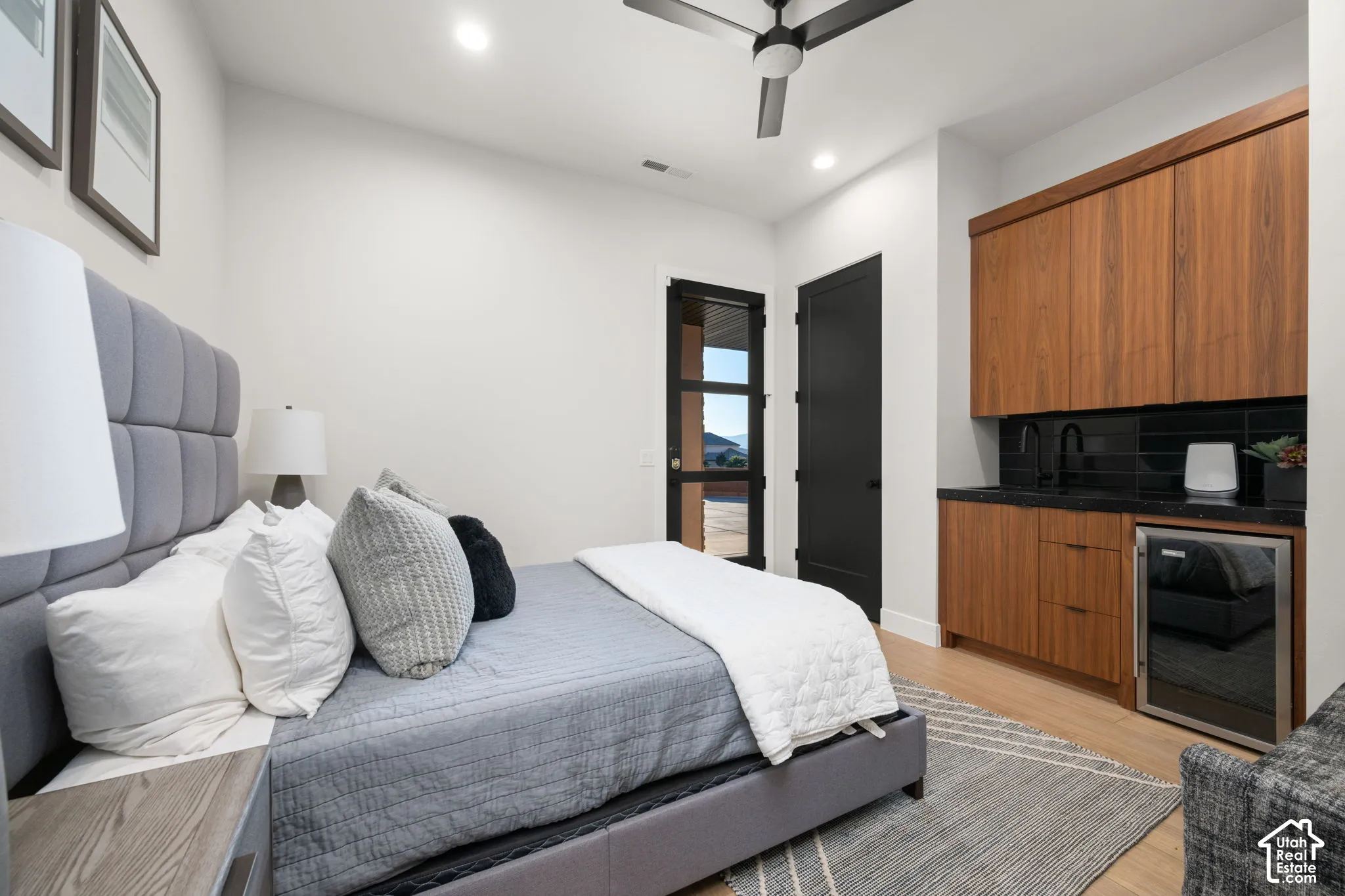 Built-in wood cabinetry featuring a dark countertop, integrated sink, and under-counter beverage refrigerator, complemented by a matte black ceiling fan and glass-paneled exterior door