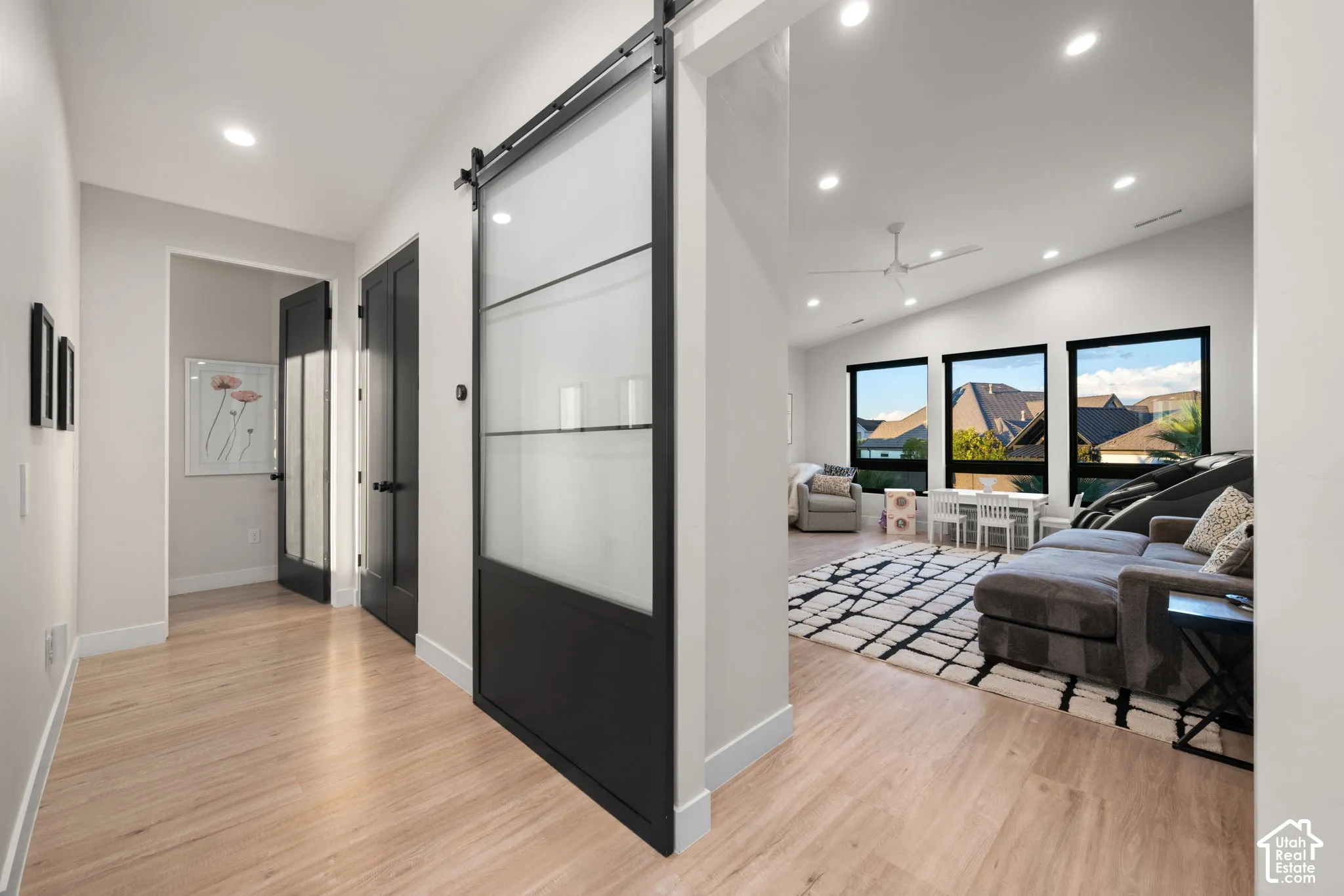 Interior featuring wood-finish flooring, a matte black sliding barn door with frosted glass panels, recessed lighting, and expansive windows with black frames