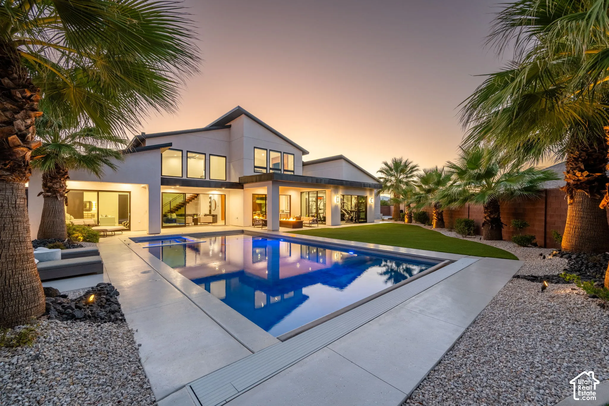 Contemporary exterior featuring a swimming pool with integrated spa, manicured turf, palm landscaping, and concrete hardscaping