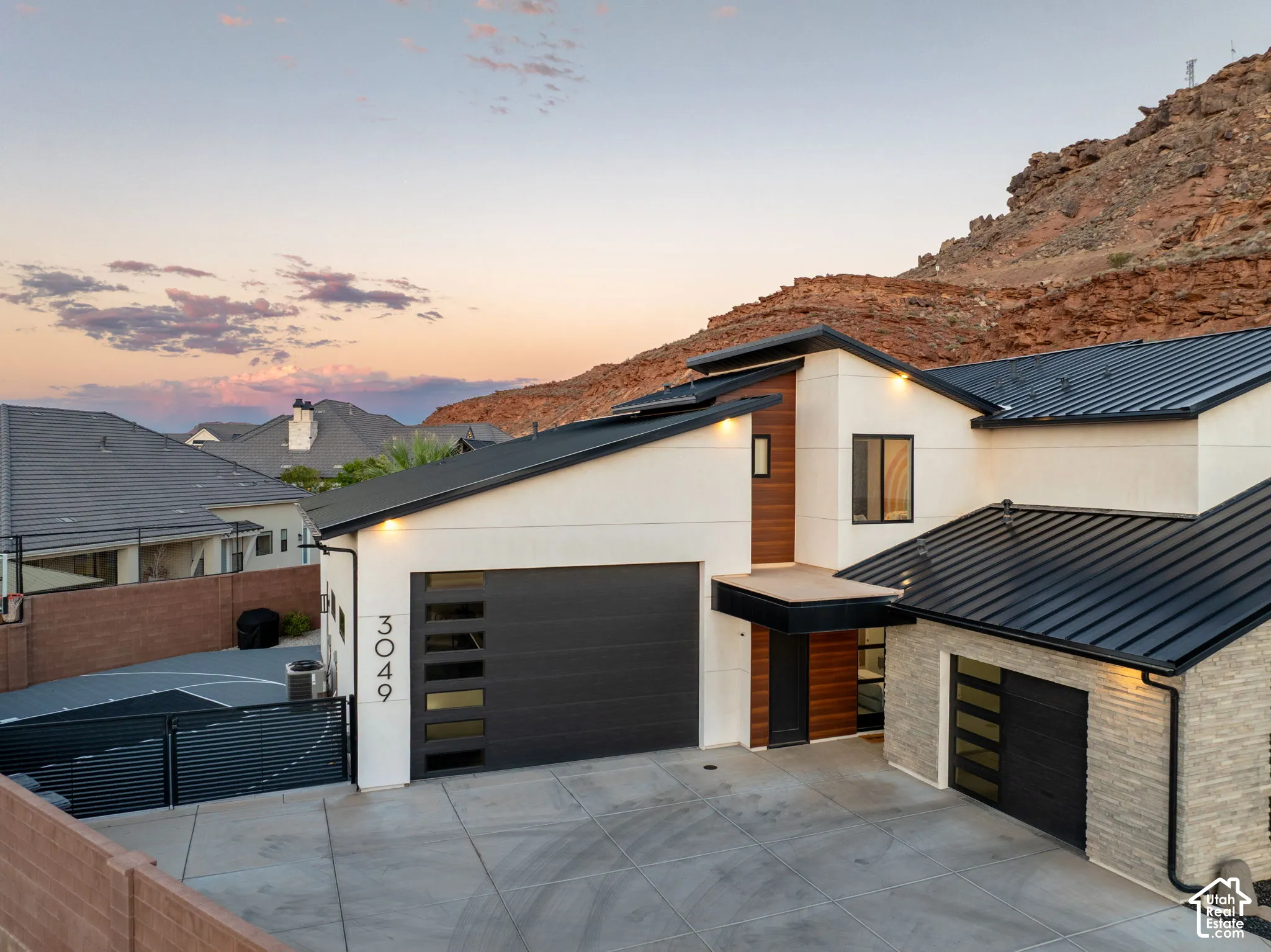 Contemporary exterior featuring smooth stucco finish, metal shed-style roofing, stone veneer accents, multi-panel garage doors with horizontal glass insets, and wood-paneled entry detail