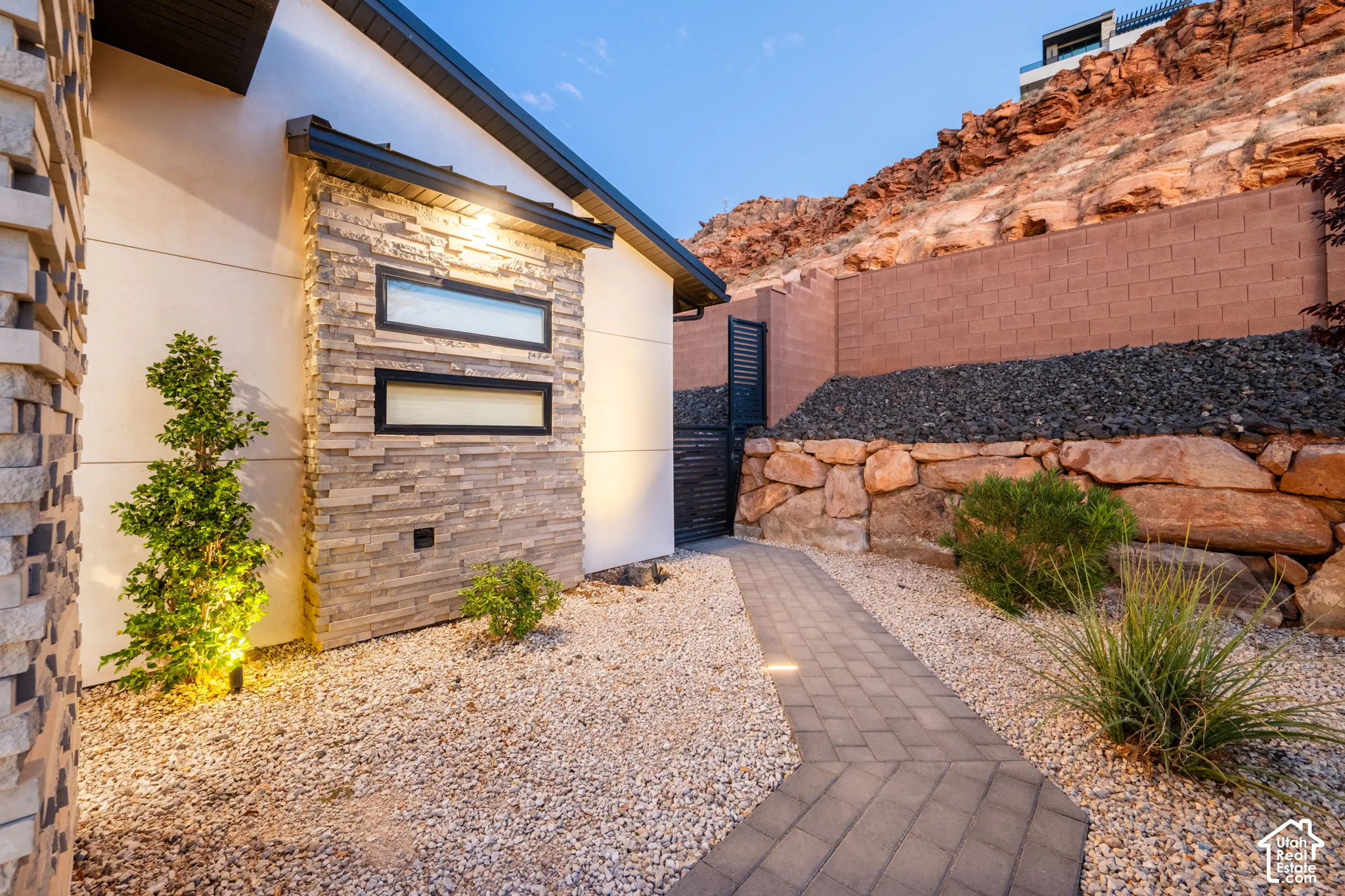 Contemporary exterior featuring stacked stone accents, horizontal clerestory windows, a paver walkway, and a tiered natural boulder retaining wall