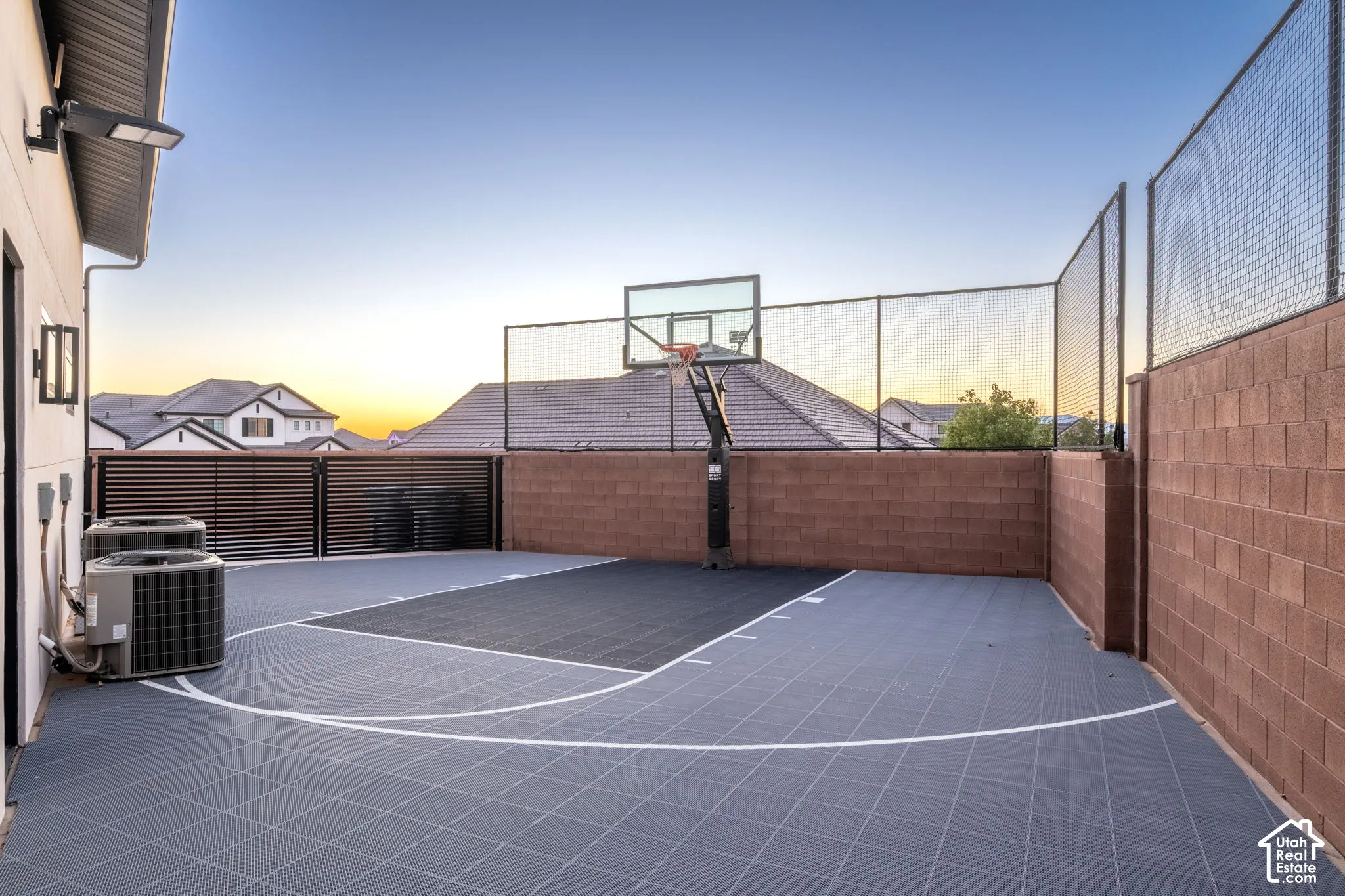 Sport court featuring modular interlocking tiles, a built-in basketball hoop, perimeter security fencing, and masonry block wall enclosures