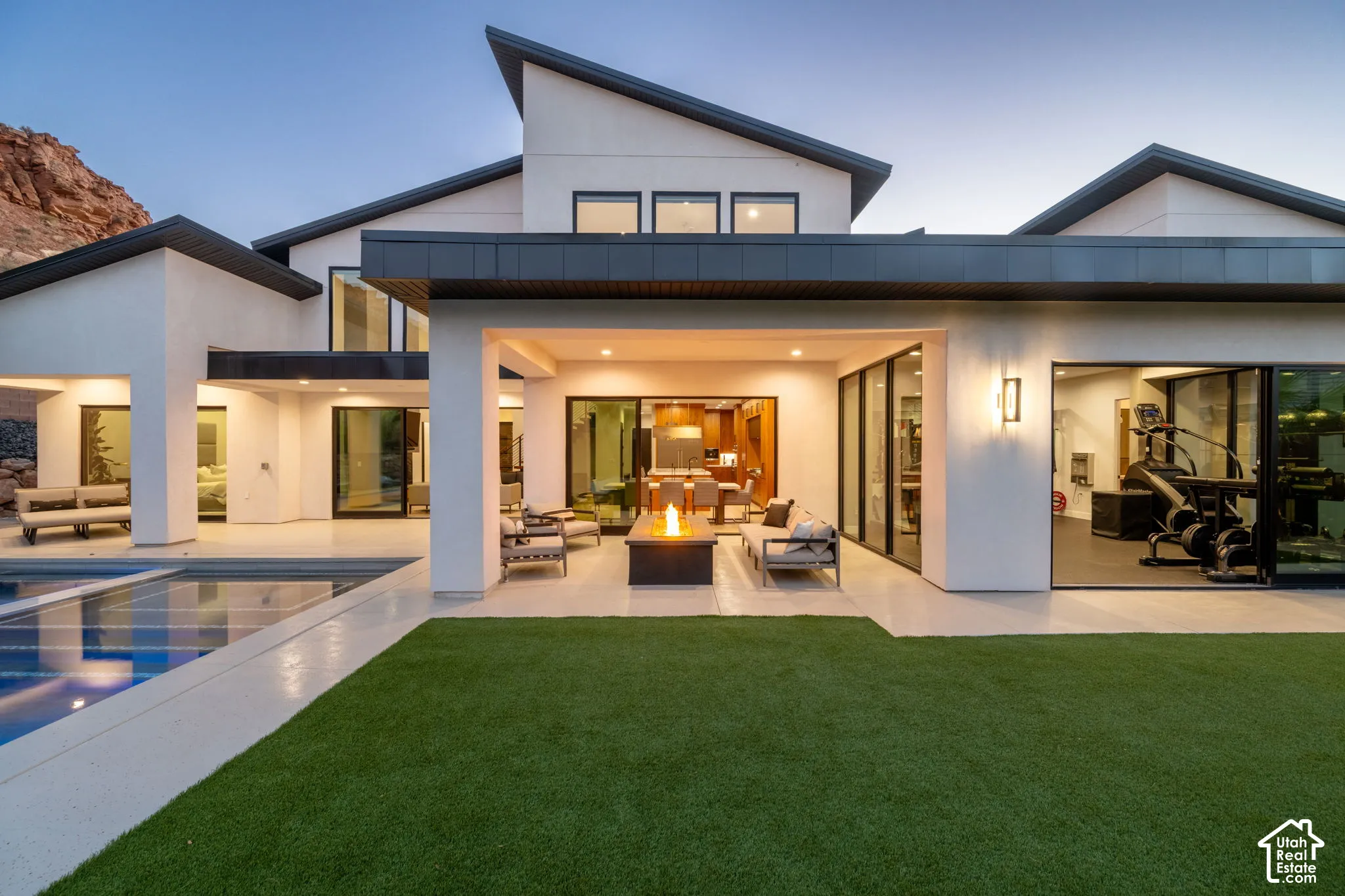 Modern exterior featuring stucco siding, multi-level rooflines, covered patio with built-in fire feature, in-ground pool, and expansive sliding glass wall panels