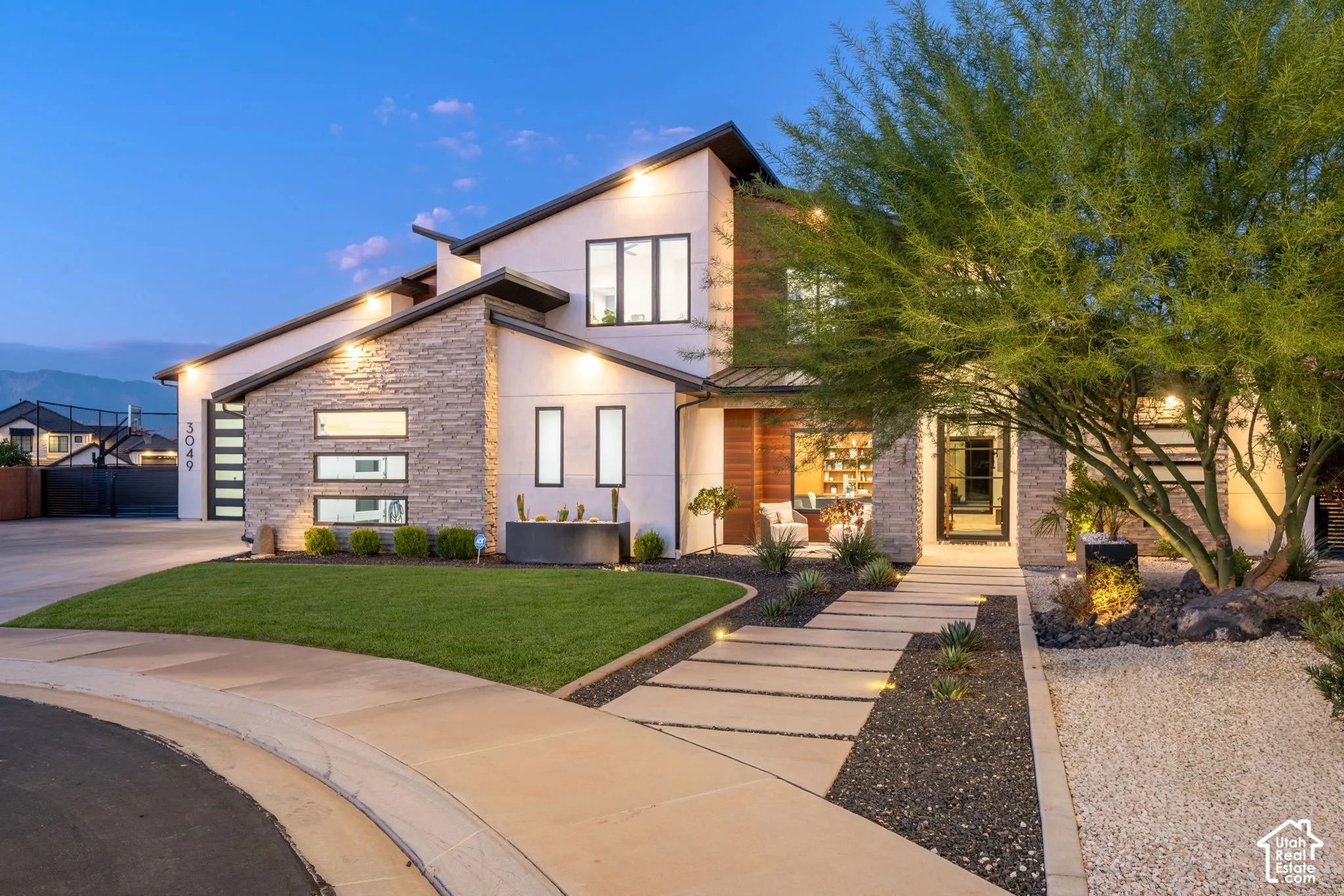 Contemporary exterior featuring multi-textured facade with stone veneer and horizontal wood siding, large multi-pane windows, paved walkway, and manicured landscaping
