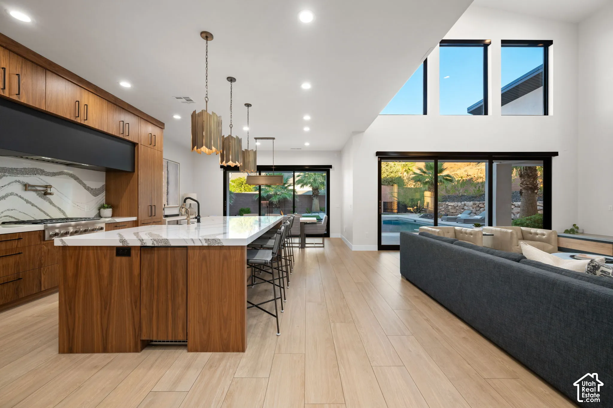 Kitchen featuring wood-finish cabinetry, stone-surface waterfall island, multi-level ceiling with recessed lighting, and expansive glass sliding doors