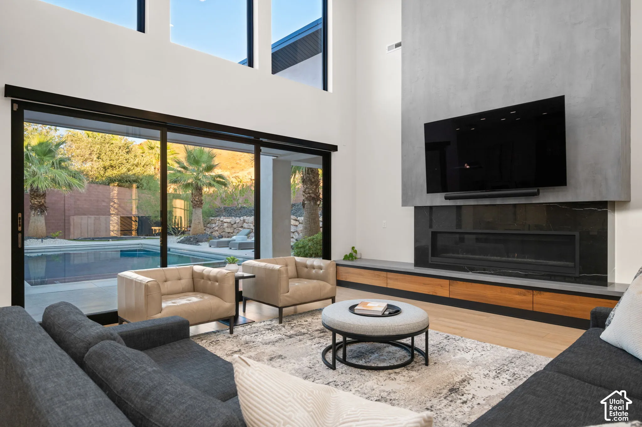 Double-height ceilings, floor-to-ceiling sliding glass doors, full-height masonry fireplace surround, built-in wood-finish cabinetry, and inset linear hearth
