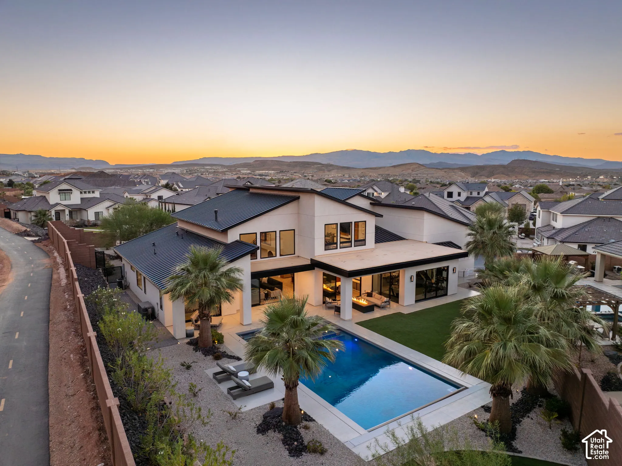 Contemporary multi-level residence featuring a metal roof, swimming pool, manicured lawn, covered patio with built-in fire feature, and mountain backdrop