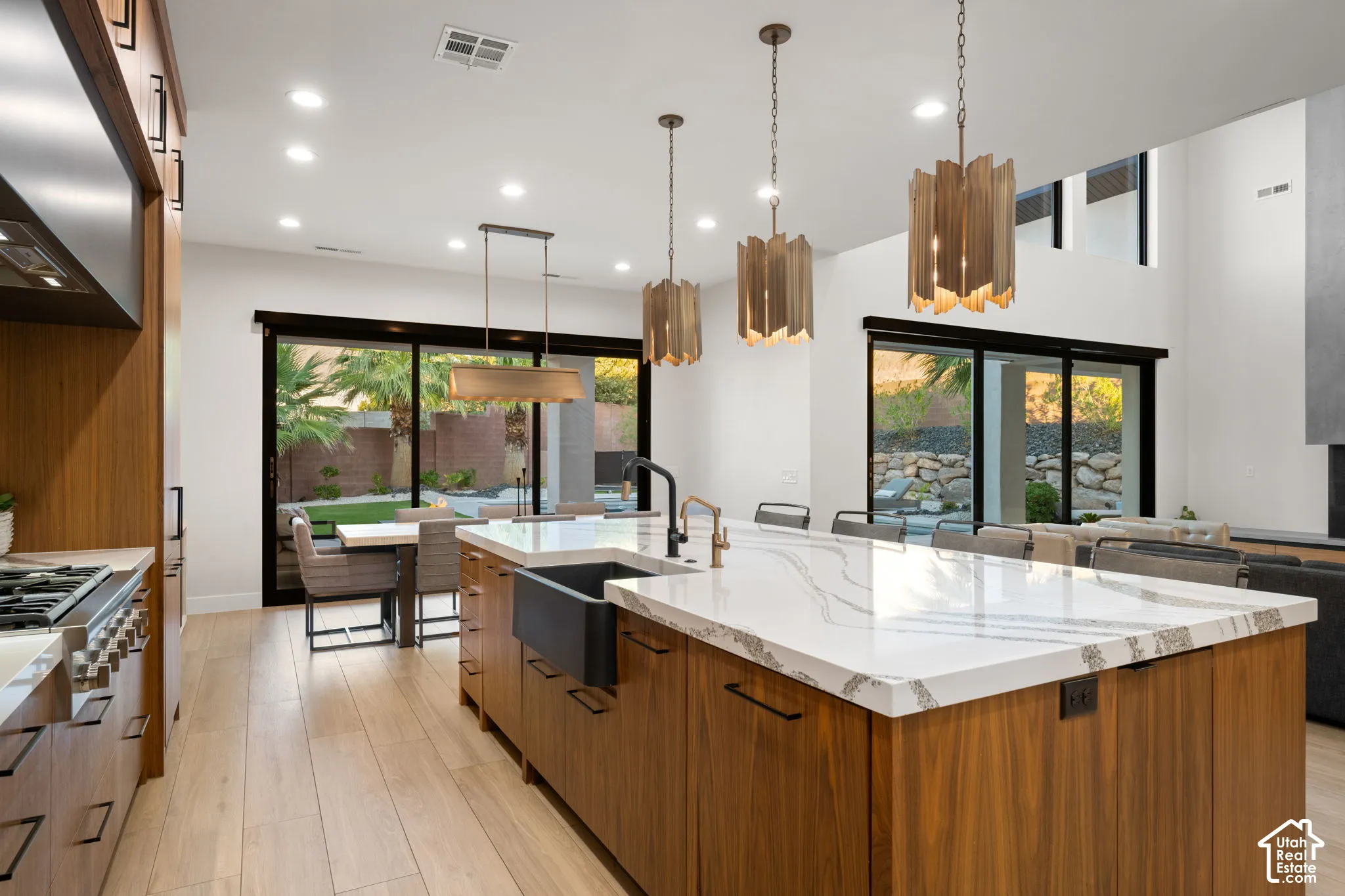 Kitchen featuring a large central island with quartz countertops, custom wood-finish cabinetry, a farmhouse-style sink, matte black hardware, and tiered metal pendant lighting