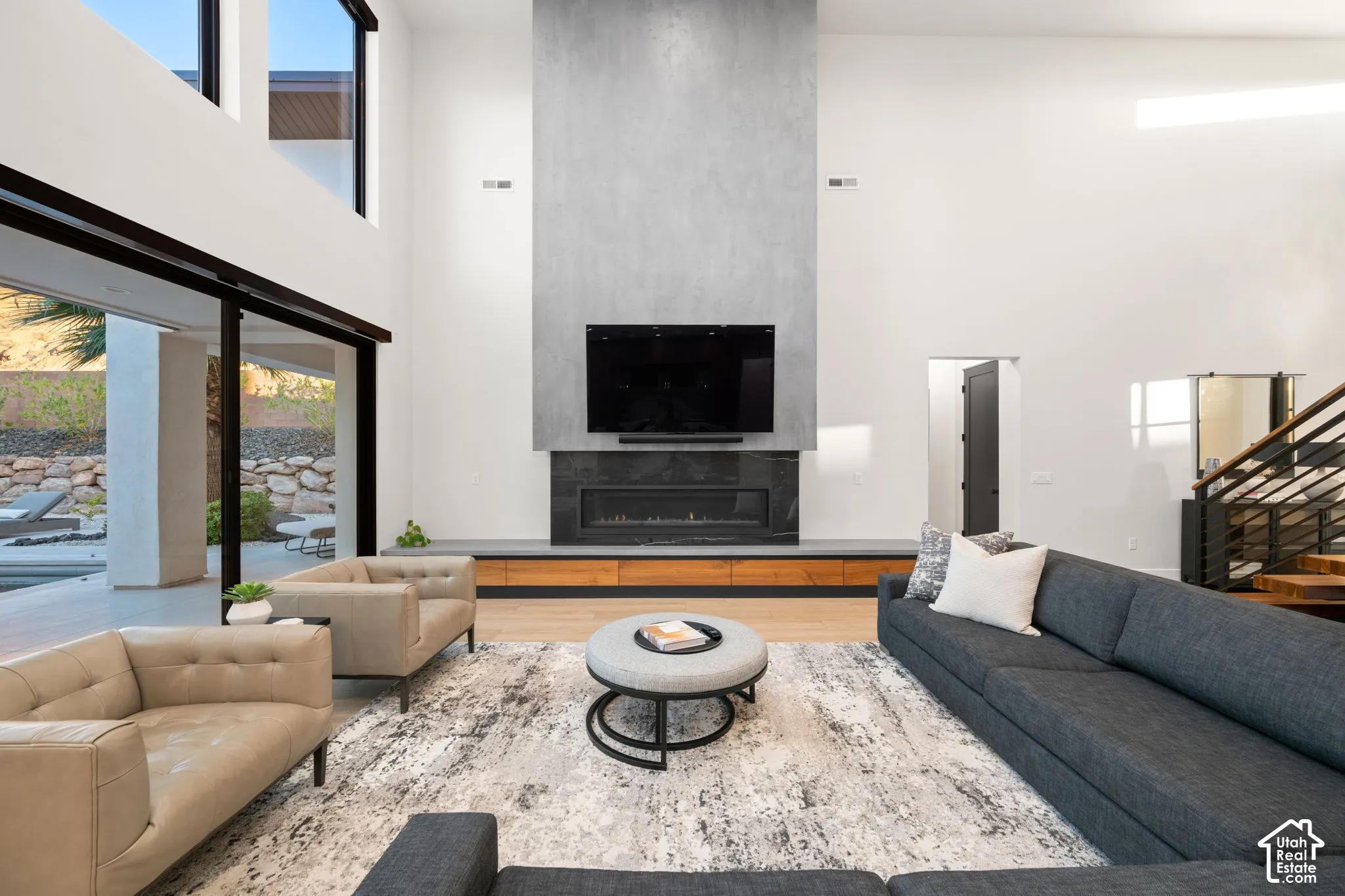 Double-height ceiling, floor-to-ceiling windows, full-height masonry fireplace surround, linear gas hearth with wood-finish built-in cabinetry, and wood-finish flooring