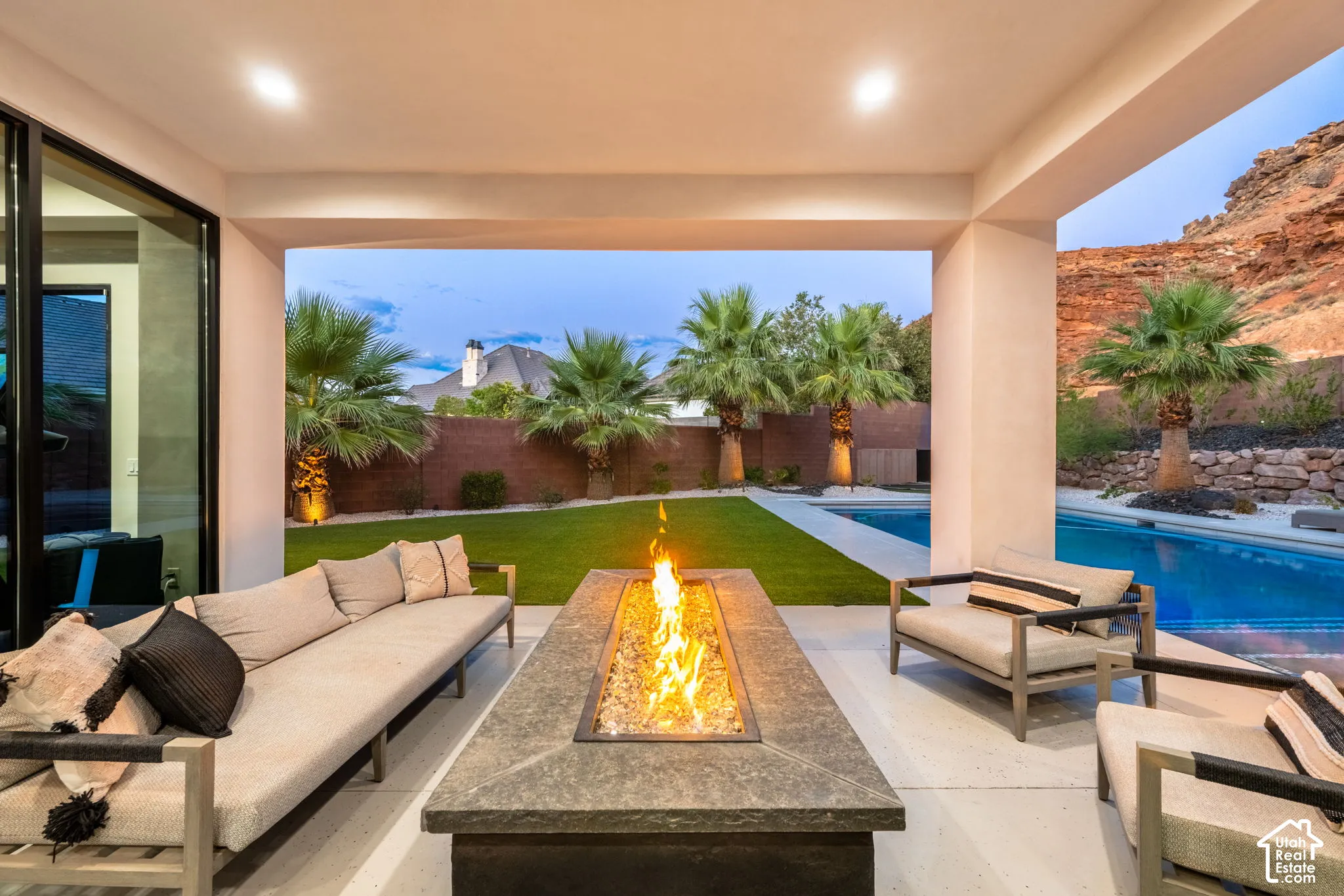 Covered patio featuring a built-in stone fire pit, swimming pool, manicured lawn, and landscape lighting