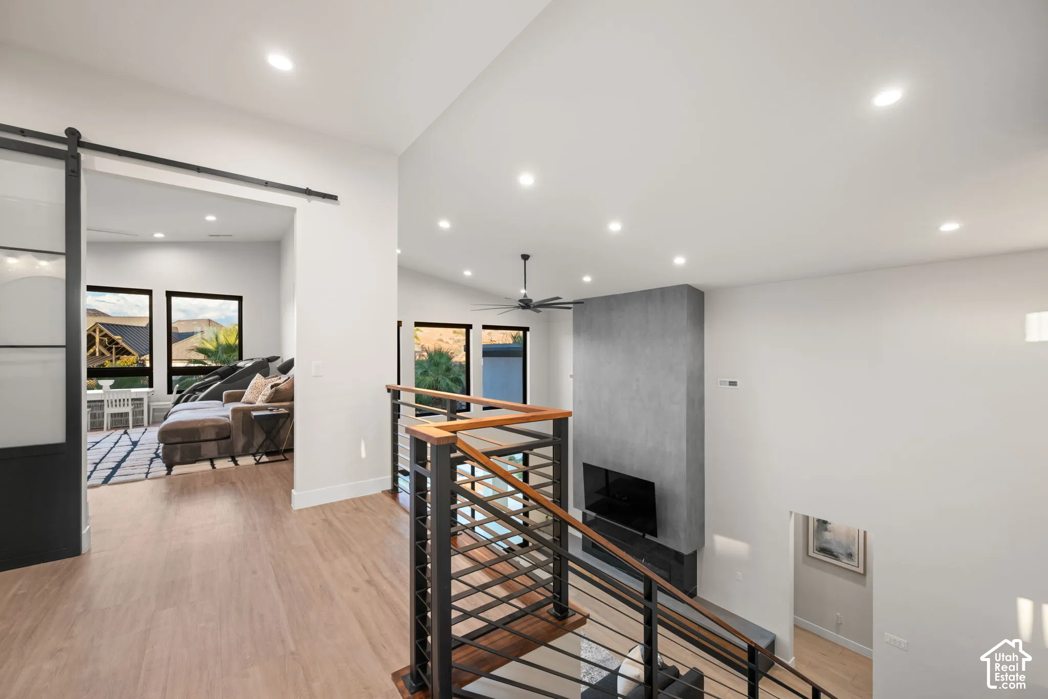Open-concept landing featuring wood-finish flooring, a metal stair railing with a wooden handrail, a floor-to-ceiling fireplace surround, recessed lighting, and a sliding glass door with a black frame