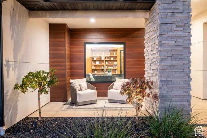 Covered entryway featuring stacked stone columns, horizontal wood-finish siding, smooth stucco finish, and a large fixed-pane window