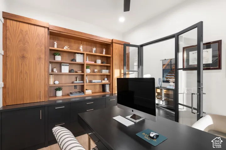 Custom built-in cabinetry with natural wood shelving and matte black lower storage, complemented by black-framed glass swing doors and a ceiling-mounted fan