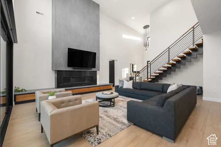Double-height ceiling, floor-to-ceiling concrete-finish fireplace, wood-finish flooring, and floating staircase with metal railing